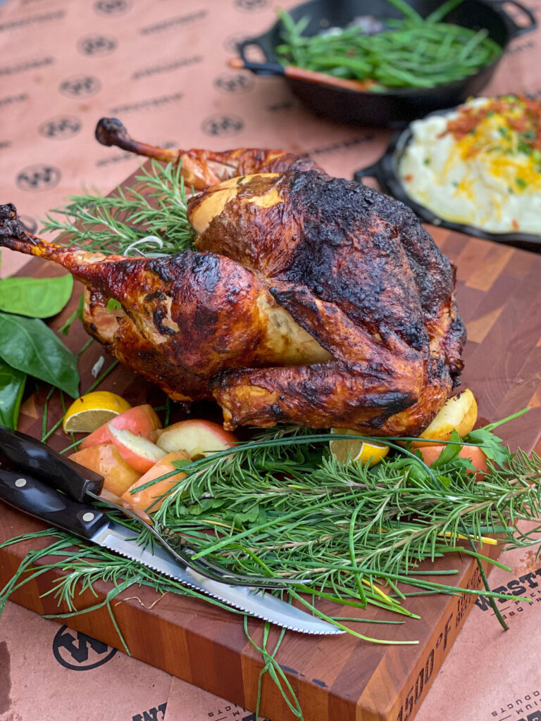 A smoked turkey is on a platter with rosemary and apples.