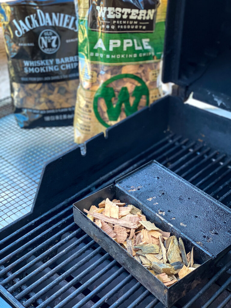 A gas grill with a smoker box of wood chips.