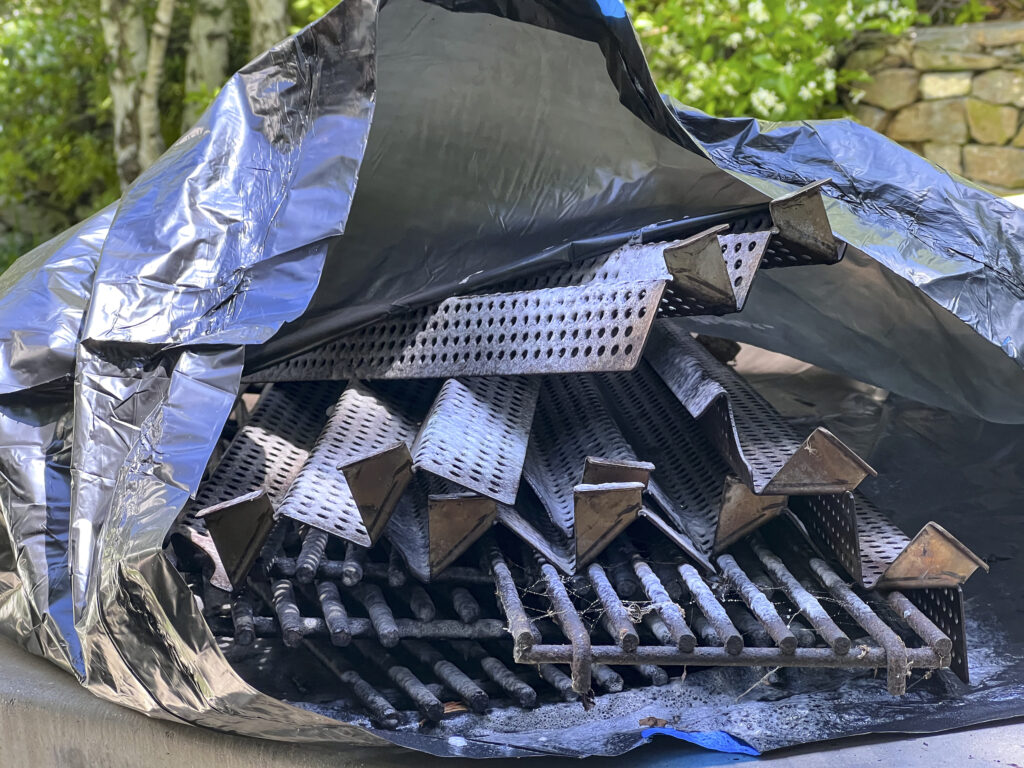 An extra large plastic bag holding grill grates and parts that have been sprayed with cleaner.