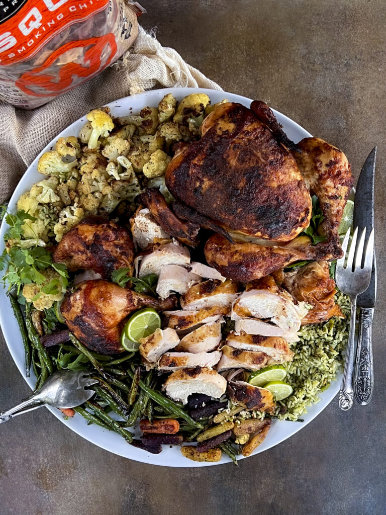 A platter of rotisserie chicken with green beans, cauliflower, and green rice.