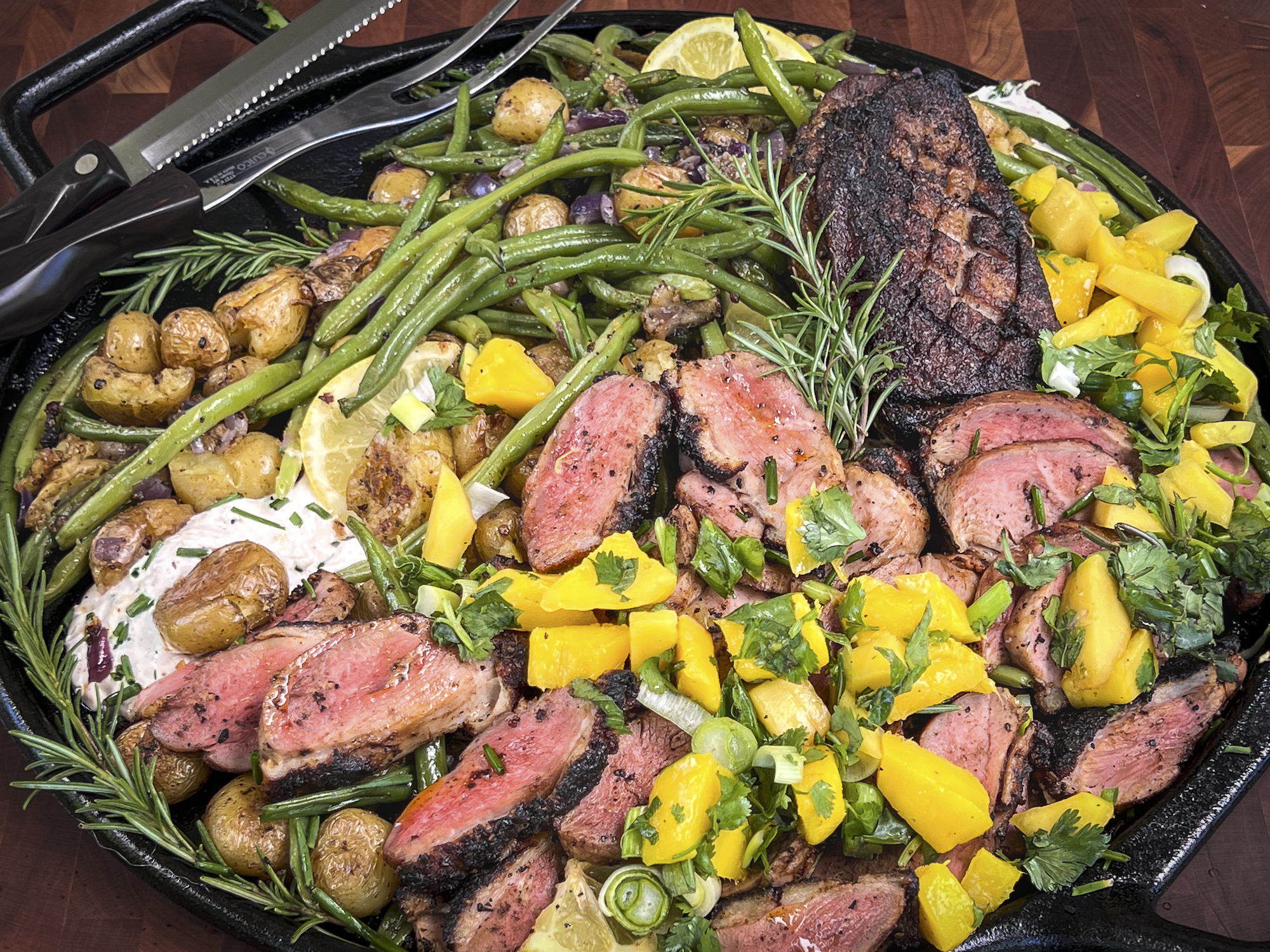 A platter of sliced smoked duck with mango, green beans, and golden potatoes.