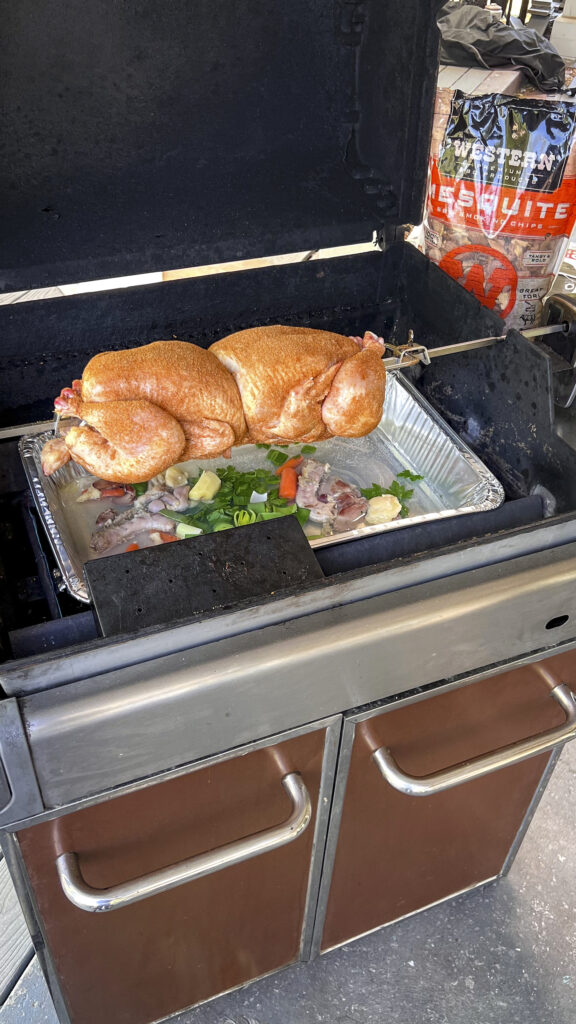 Two chickens on on the rotisserie with a drip pan underneath. 