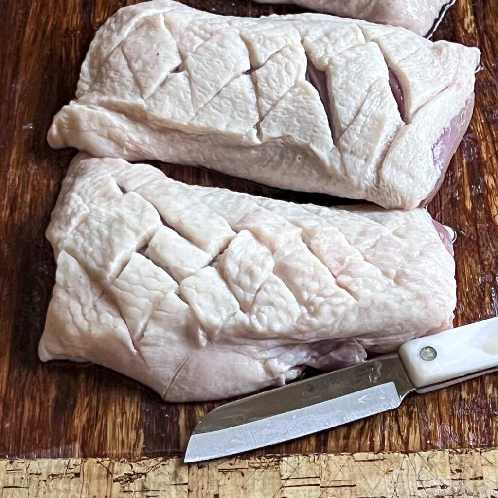 Two duck breasts are scored by cutting skin in a diamond pattern.