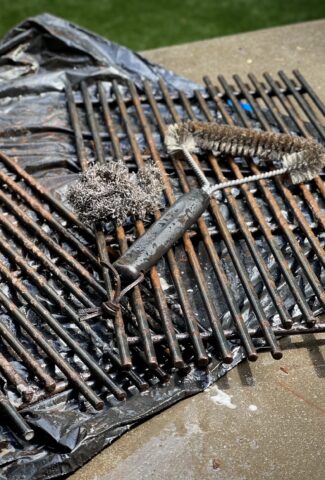 Dirty grill grates that need scrubbing! A wire brush and steel scrubby are on the grates ready to be used.