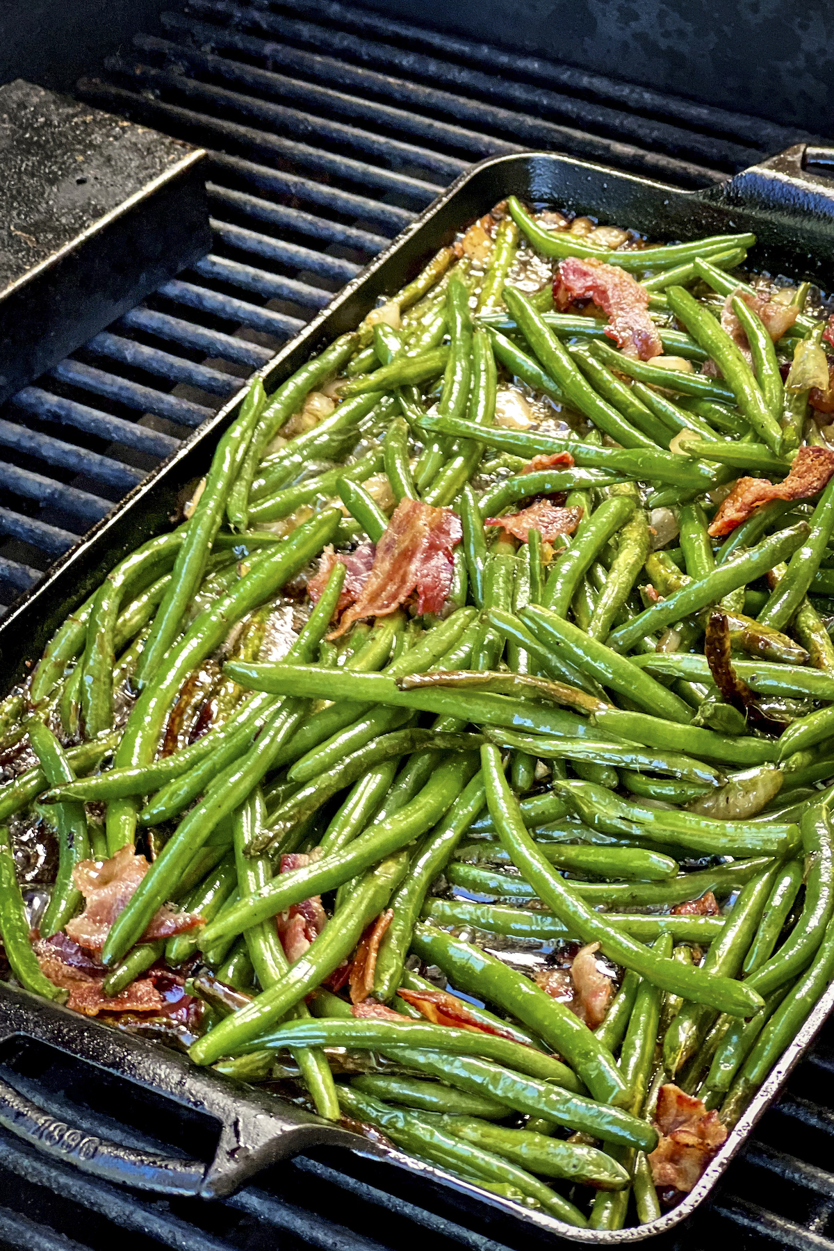 Green Beans with Bacon are in a cast iron pan on the grill.