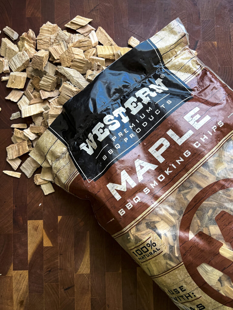 Western Maple BBQ Smoking Chips fall out of a bag and onto a wood cutting board.