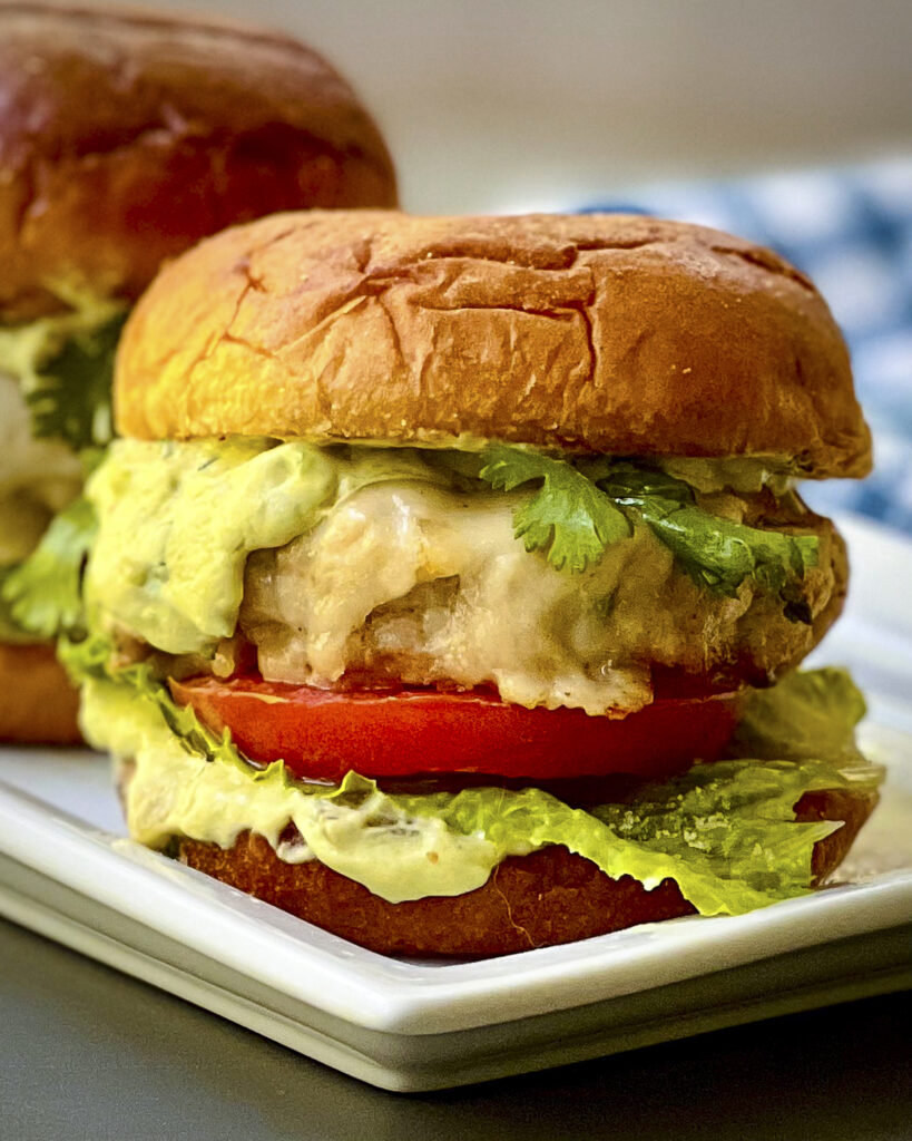 A close up of a chicken burger with avocado spread and a tomato. 