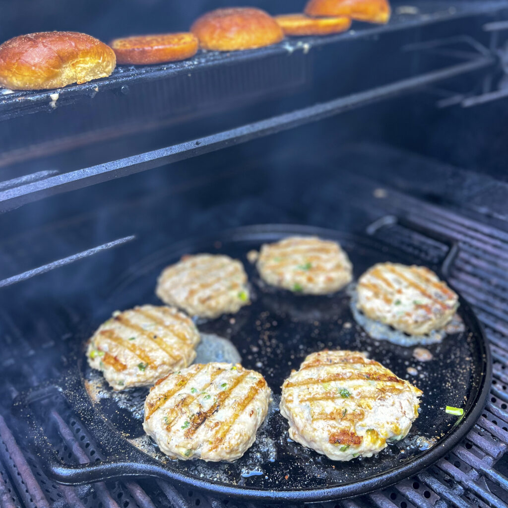 Six chicken burgers are on cast iron pizza pan inside a grill.