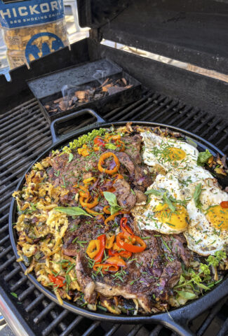 A cast iron skillet has smoked and grilled hash browns, rib eye steaks and eggs.