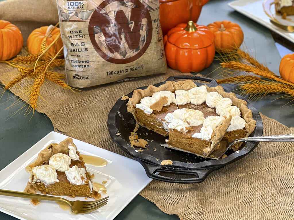 A smoked pumkin pie is sliced and one pie is on a white dessert dish. Western BBQ Smoking Chips are in the back to show what type of smoke. 