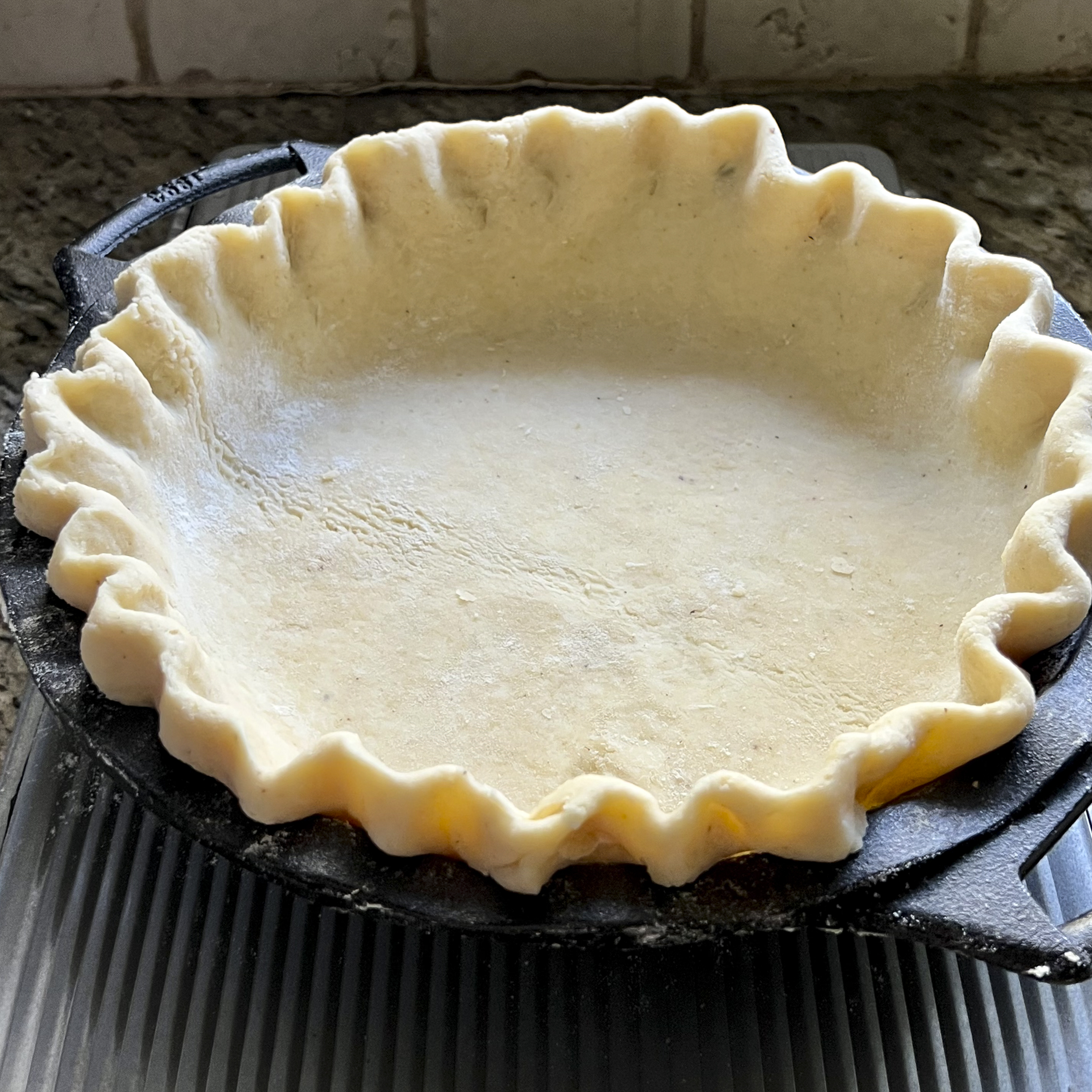 An unbaked pie crust is in a cast iron pie pan.