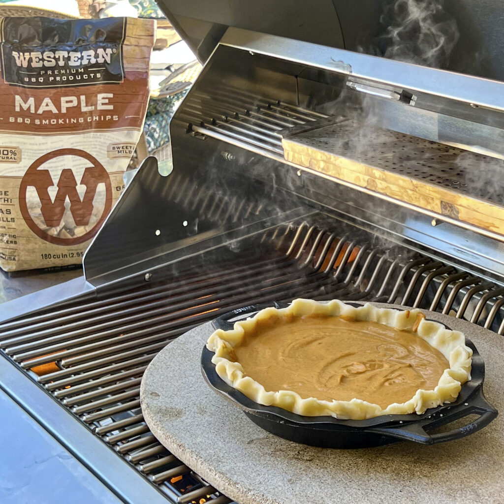 Pumpkin PIe is being baked on a baking stone on the grill. A bag of Western BBQ Maple Smoking Chips is in the backdrop.