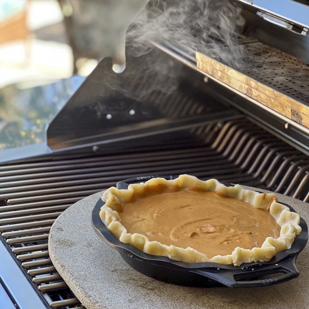 A pumpkin pie smokes on the grill. 