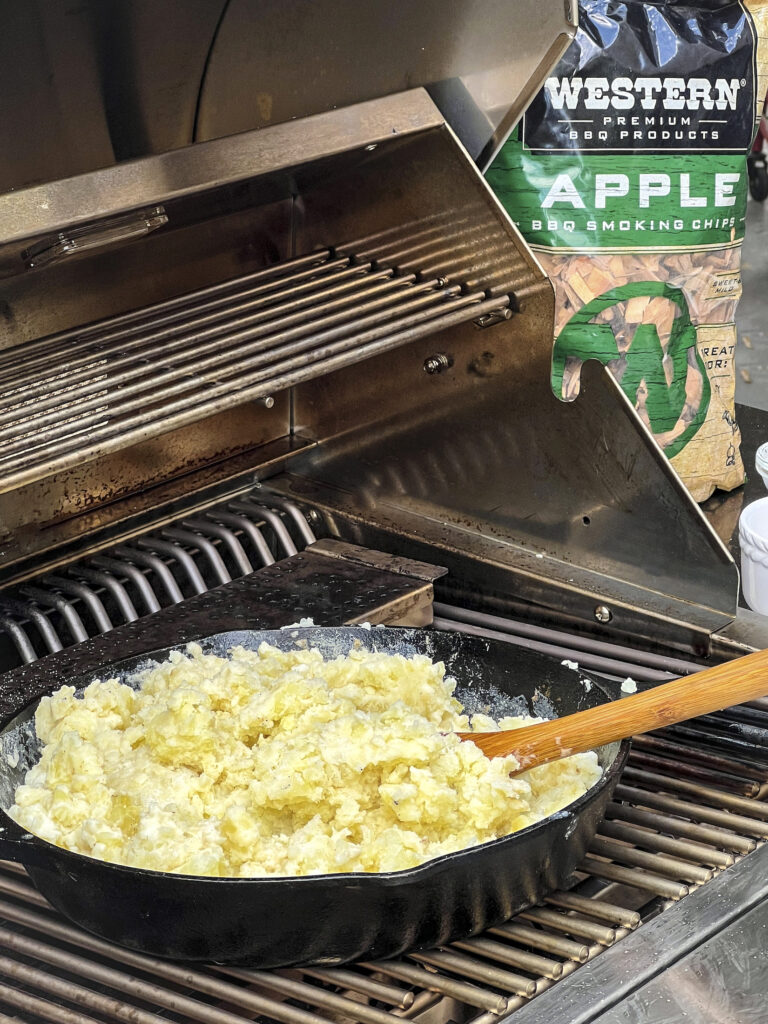A skillet of potatoes is on the grill but has no toppings.