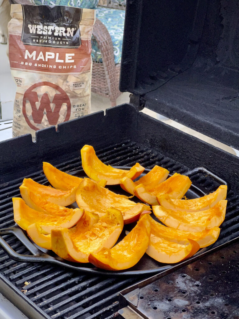 Slices of pumpkin are on the grill being smoked by maple smoking chips. 