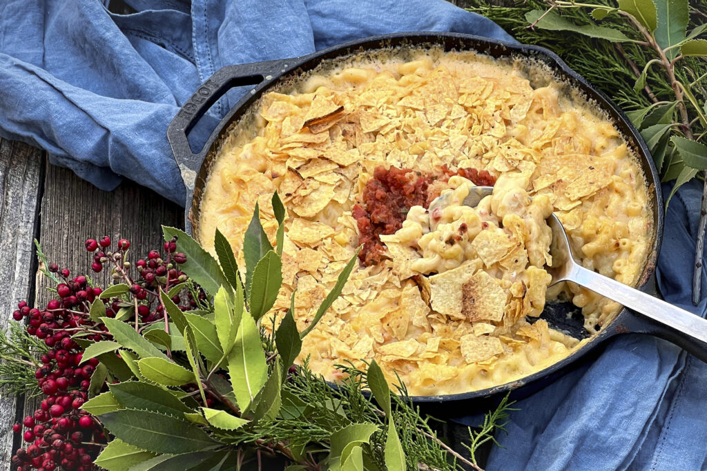 A cast iron skillet hold salsa mac and cheese. The mac and cheeses has a topping of toasted crushed tortilla chips and salsa.