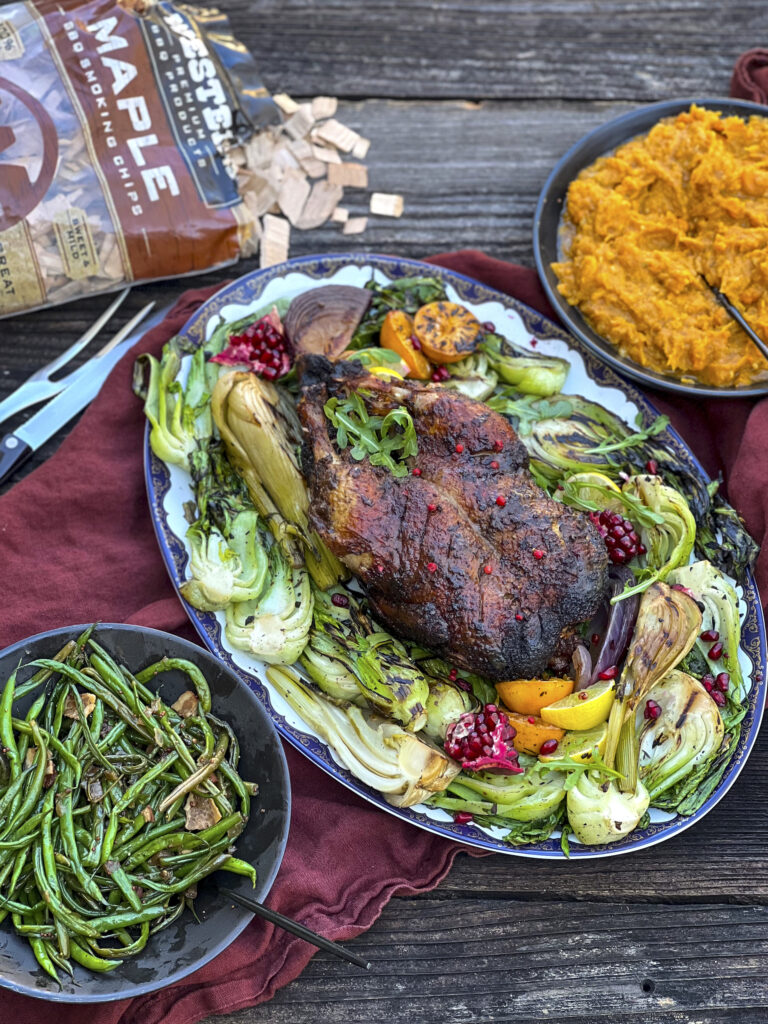 A holiday meal is on a wood table with green beans, squash, maple smoking chips, and smoked duck. 