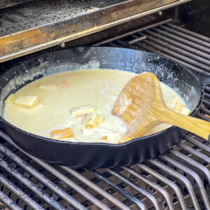 Cheese has been added to a cast iron skillet of cream sauce for Mac and Cheese. 