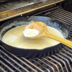 A cast iron skillet with warm milk and butter is ready for cheese to be added.