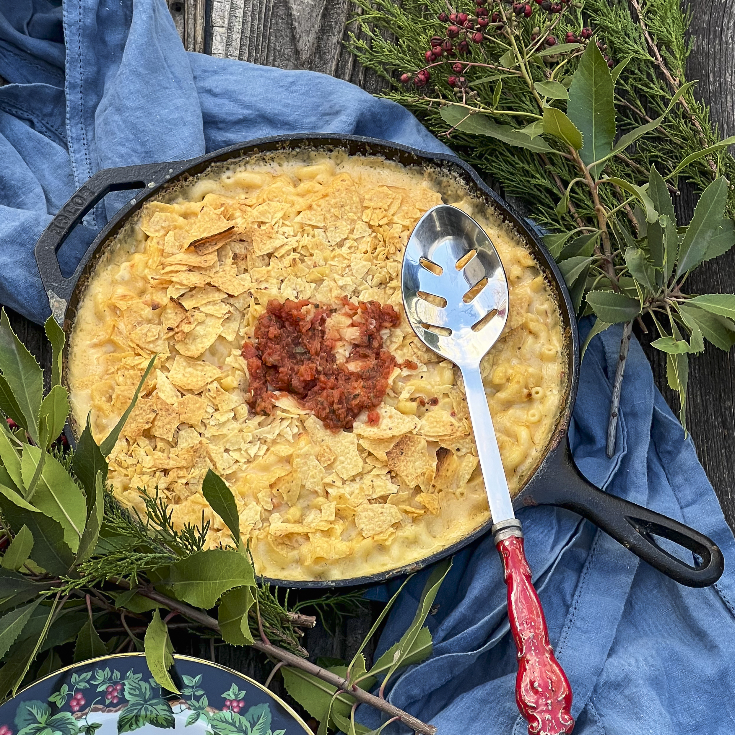 Smoked Mac and Cheese is in a cast iron skillet and served with a large red handle spoon.