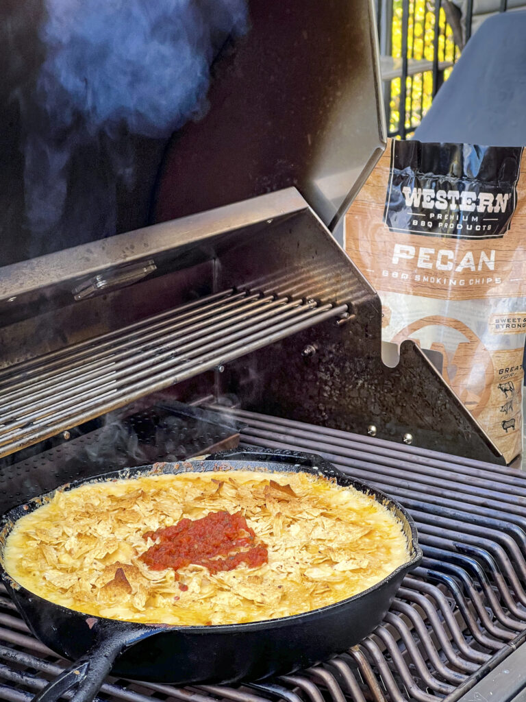 Mac and cheese with a tortilla topping is on the grill. A bag of Western BBQ Pecan smoking chips is in the background.