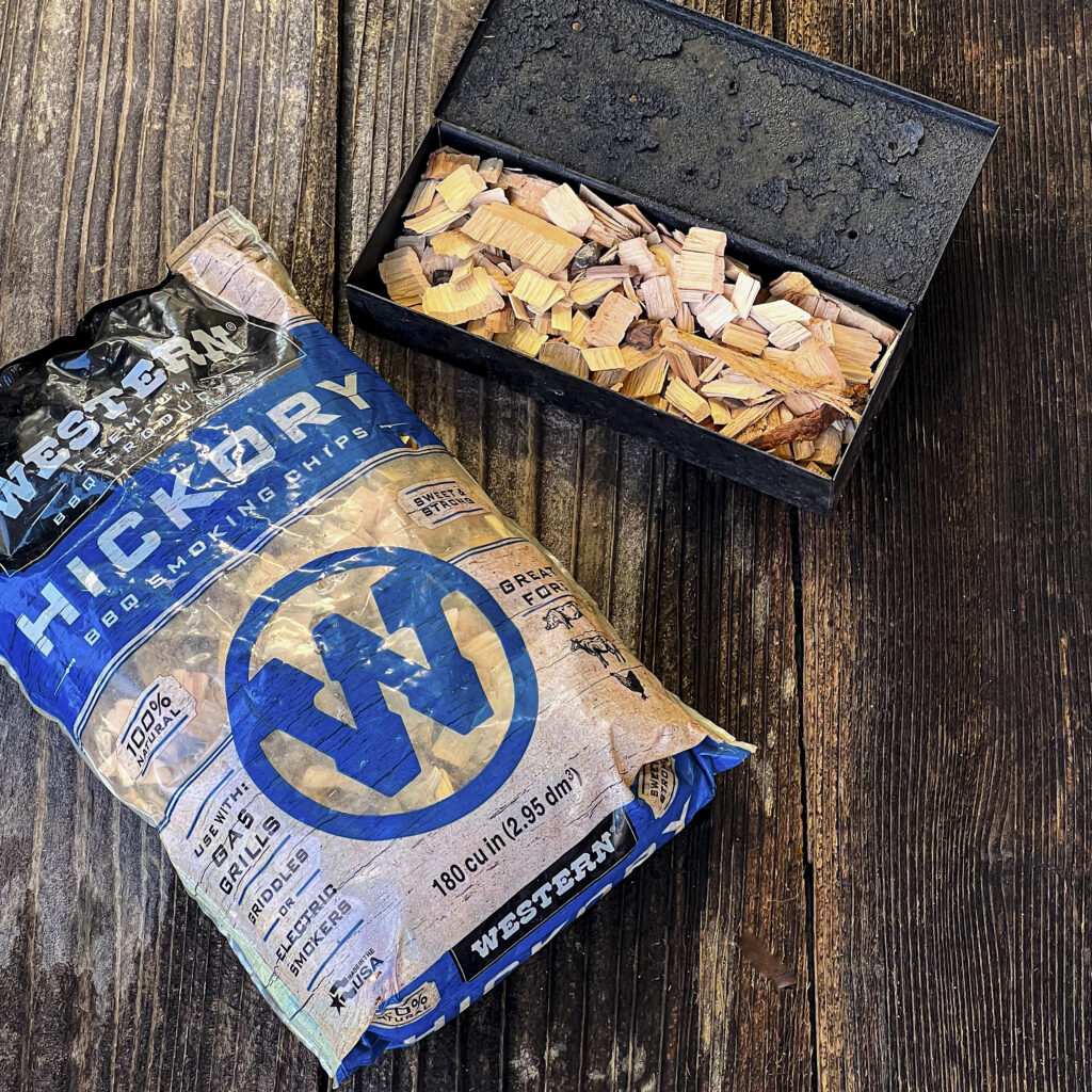 A bag of Western BBQ Hickory Chips is next to a smoker box of smoking chips.