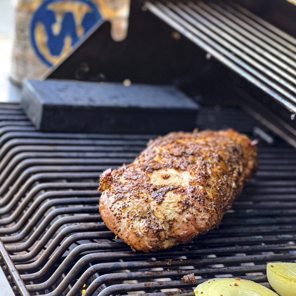 A pork loin is browned on a grill with Western BBQ  Hiclory Chips in the backdrop. 