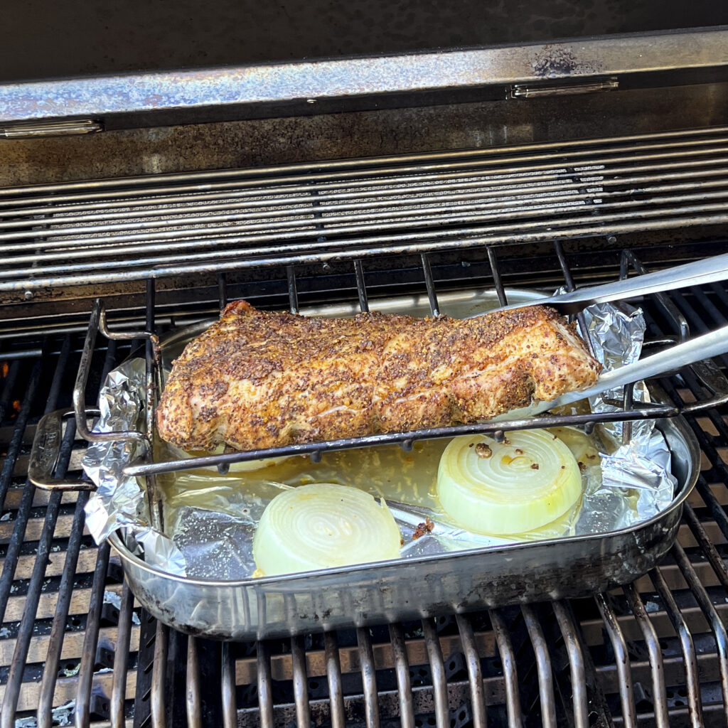 A seasoned pork loin is in a rack on the grill. The rack is in a roasting pan. 