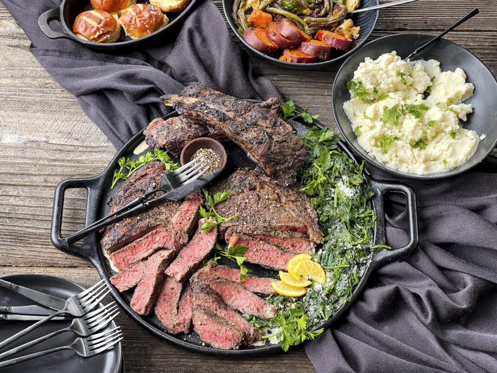 A platter of hickory smoked ribeye steak is beautifully presented with spinach and mashed potatoes. 