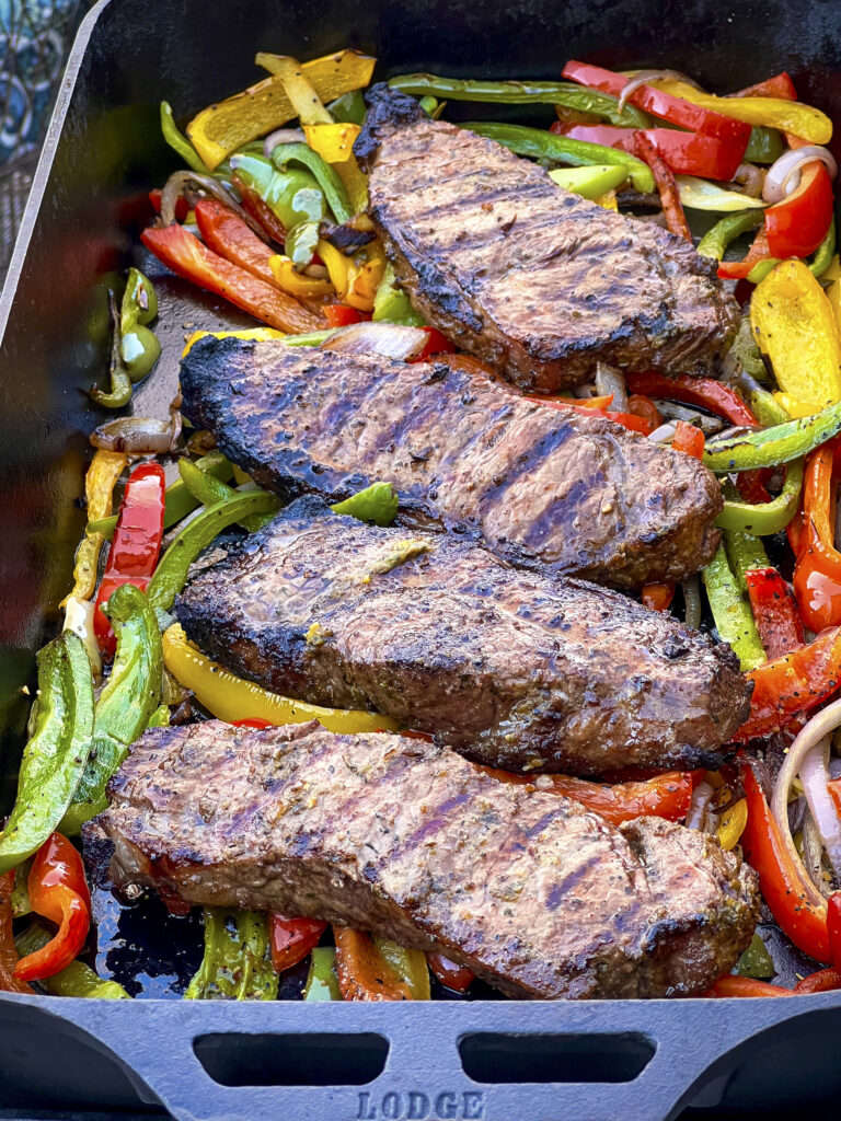 4 Strip Steaks have been smoked and grilled and placed on a cast iron pan of grilled peppers.