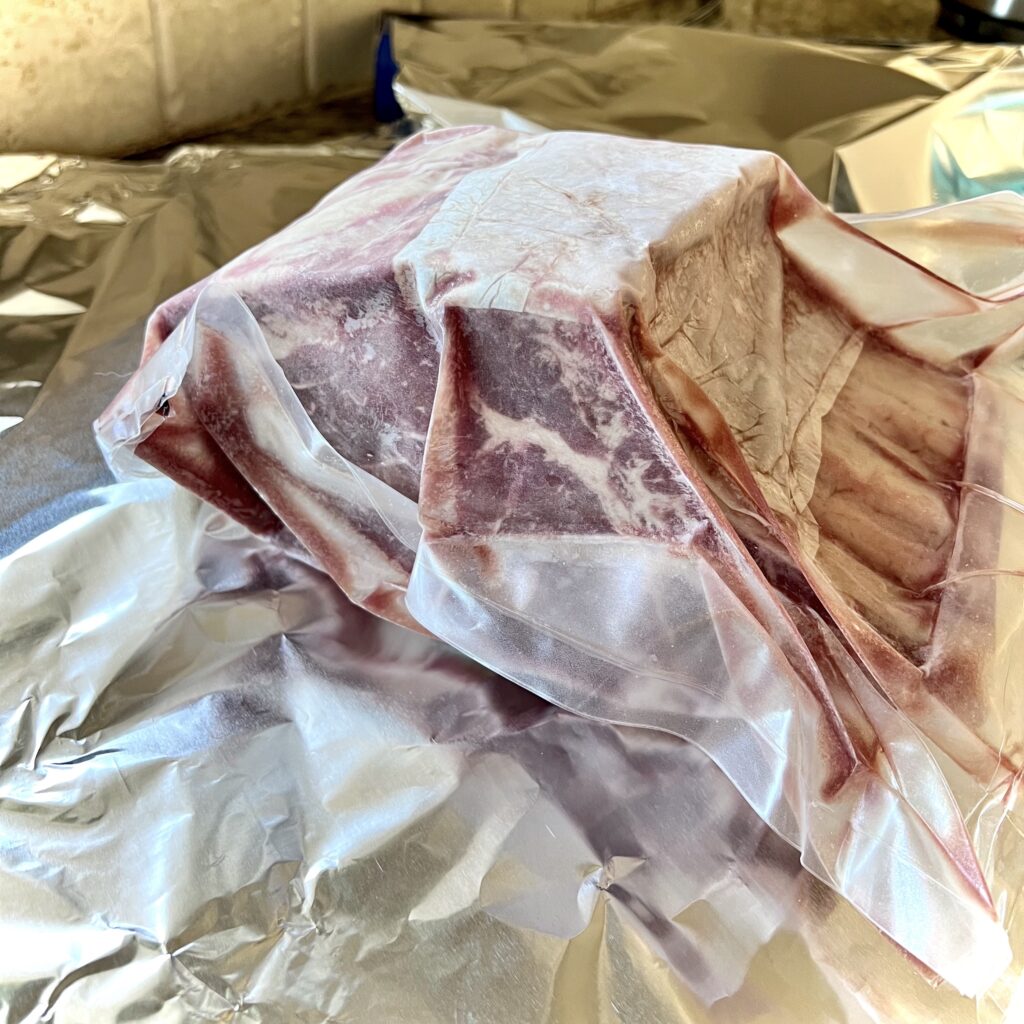 A vacuum packed bone-in ribeye roast is waiting to be foil wrapped.