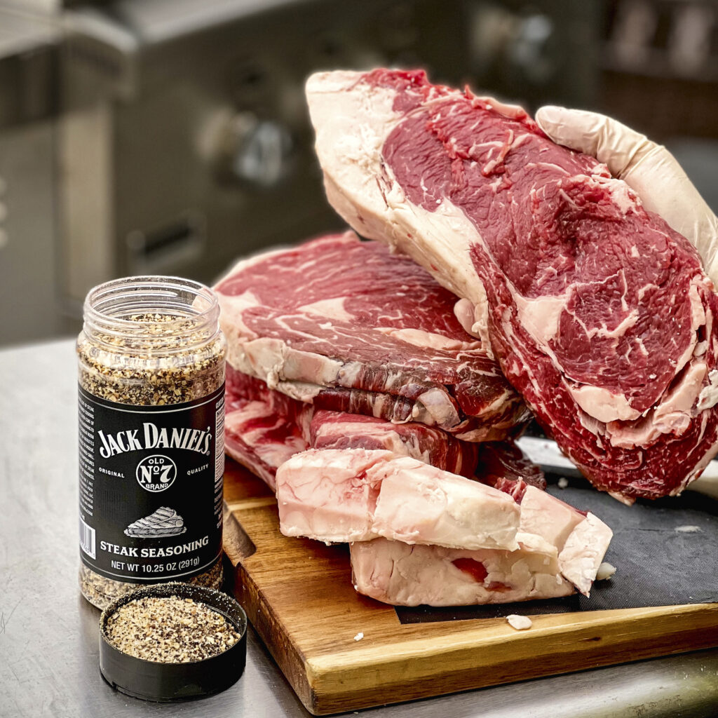A stack of steaks has been hand cut from a roast. Jack Daniel's Seasoning is nearby. 