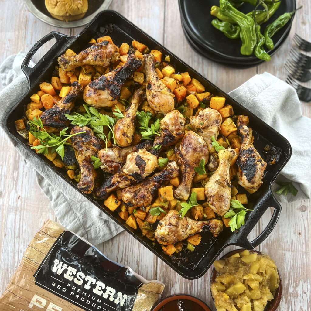A cast iron rectangular pan holds drumsticks and roasted butternut squash. 