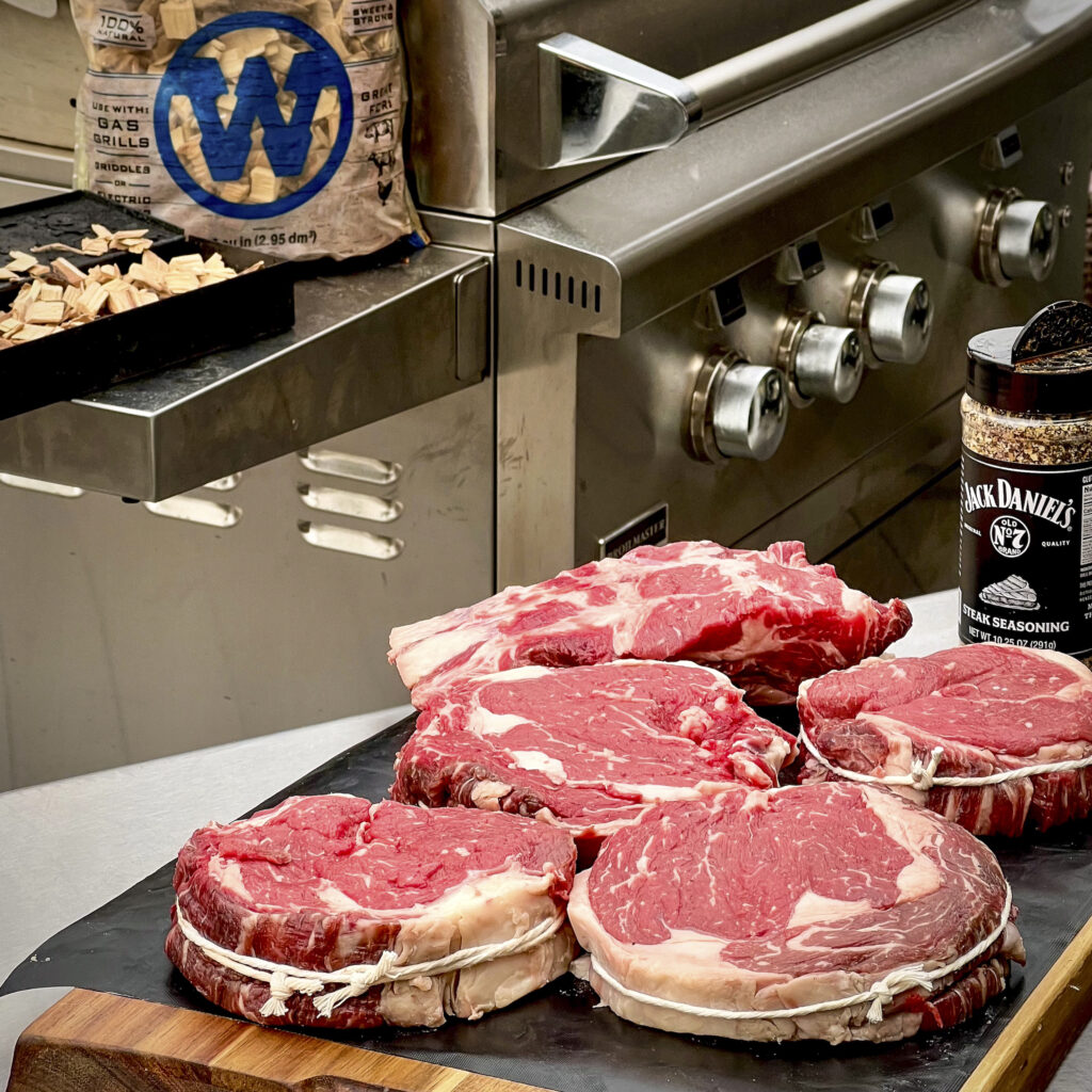 5 hand cut steaks on a cutting board with wood chips in the background. 