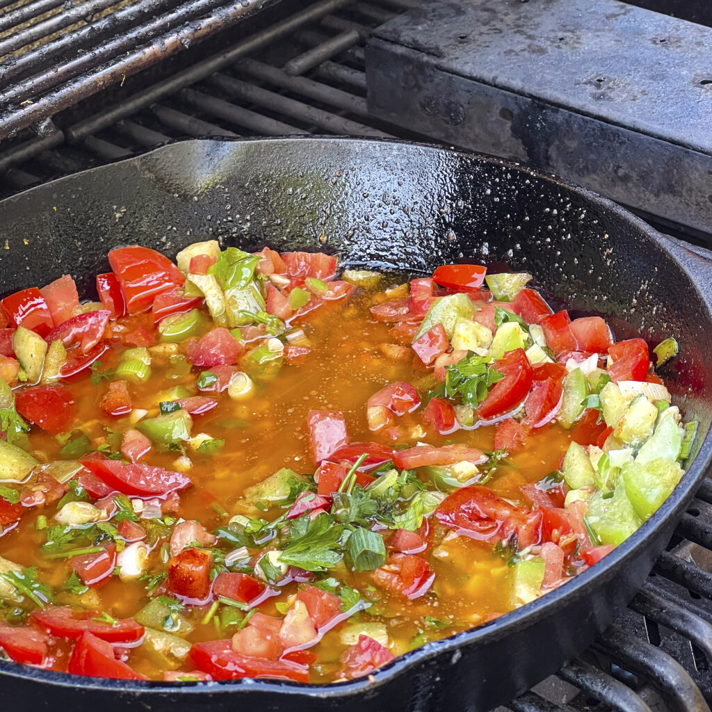 A skillet with melted butter mixed with tomatoes, tomatillos, and scallions. 