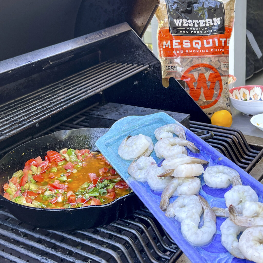 A platter of raw shrimp is about to be poured in to a skillet of tomato butter poaching sauce. 