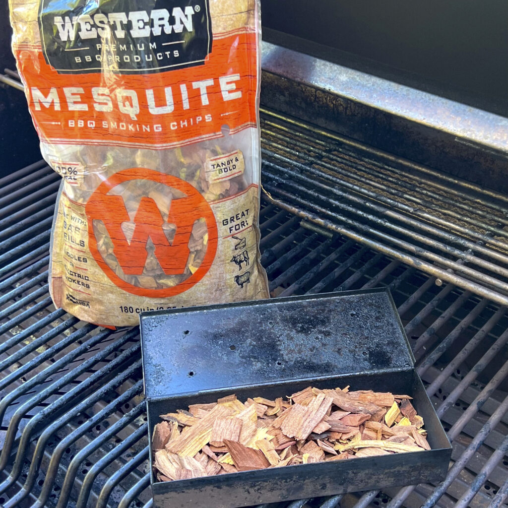 A bag of Mesquite Smoking Chips is next to a smoker box filled with mesquite smoking chips. 