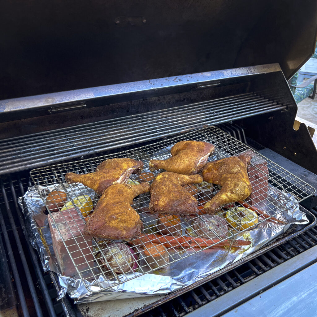 The grill is opened showing seasoned chicken leg hindquarters smoking. 