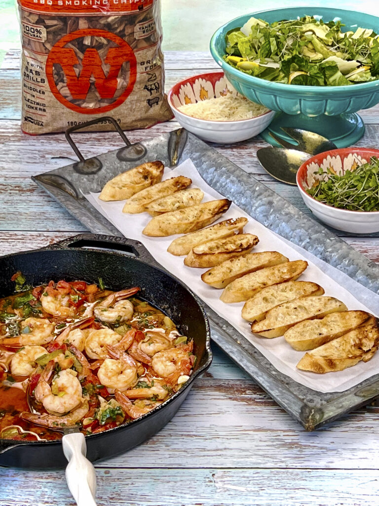 Grilled baguettes are next to a skillet of butter poached shrimp. 