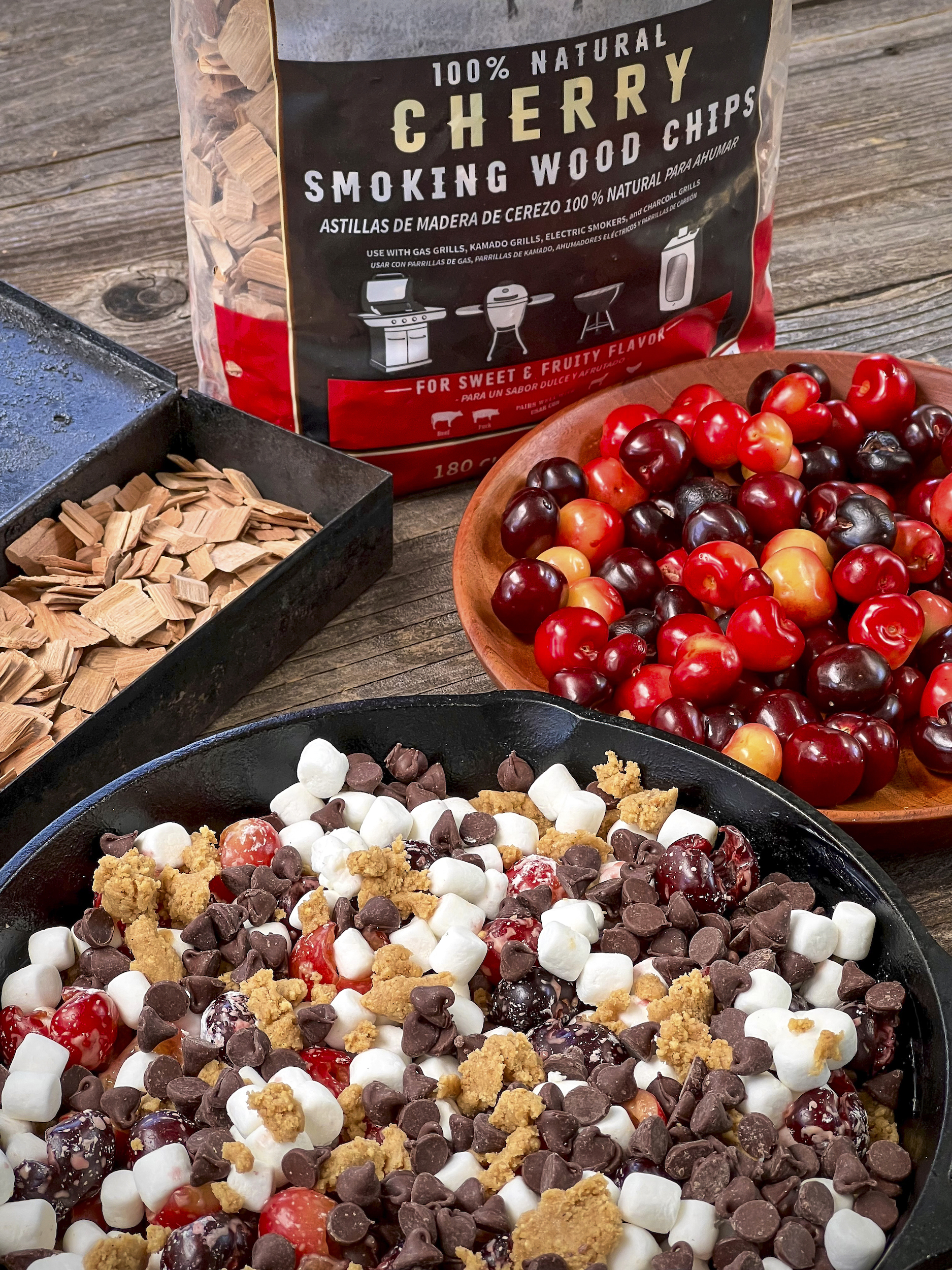 Cherry Smoking Chips are near cherries, and a skillet of a cookie bar with chocolate chips, graham cracker cookie dough, marshmallows and cherries.