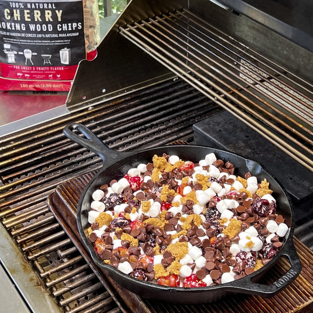 A skillet with s'mores themed ingredients is on the grill. 