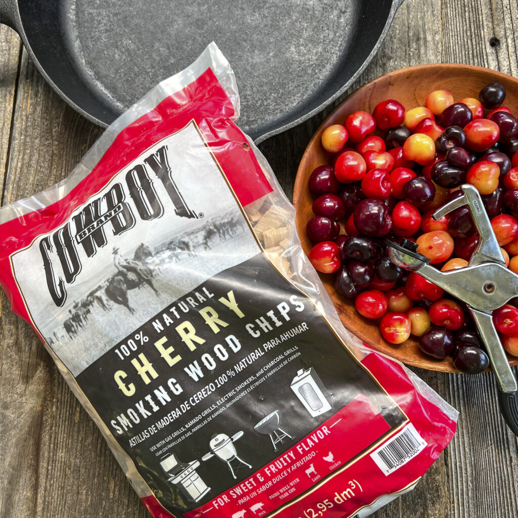 A bag of Cowboy Cherry Smoking Wood Chips sits next to a bowl of cherries.