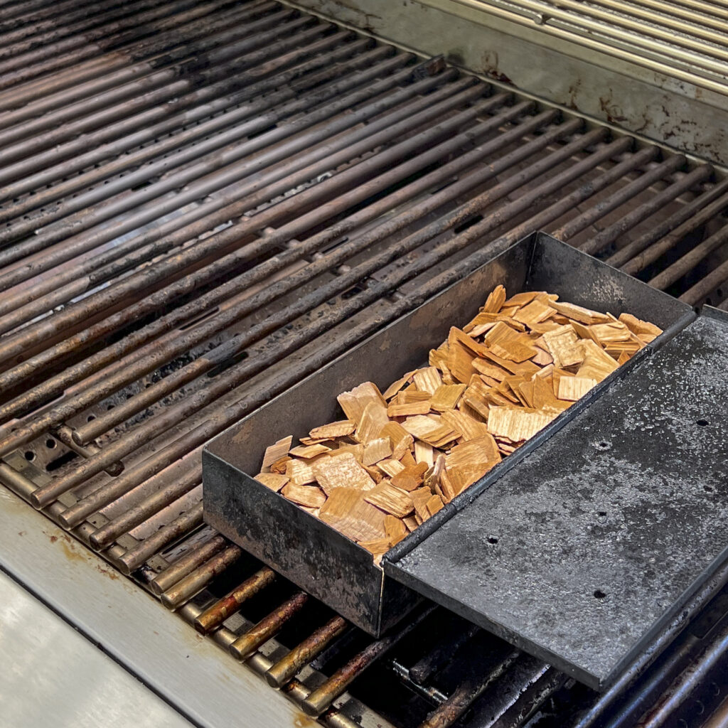 A smoker box of Cowboy Brand Cherry Smoking Chips is on the grill. 