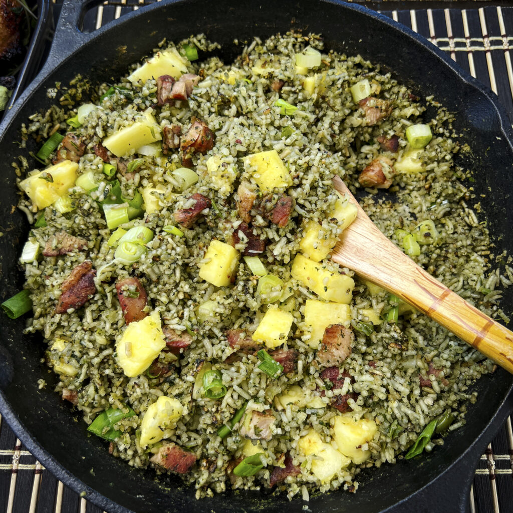 A cast iron skillet is full of green rice, pineapple, and pork is ready to be served.