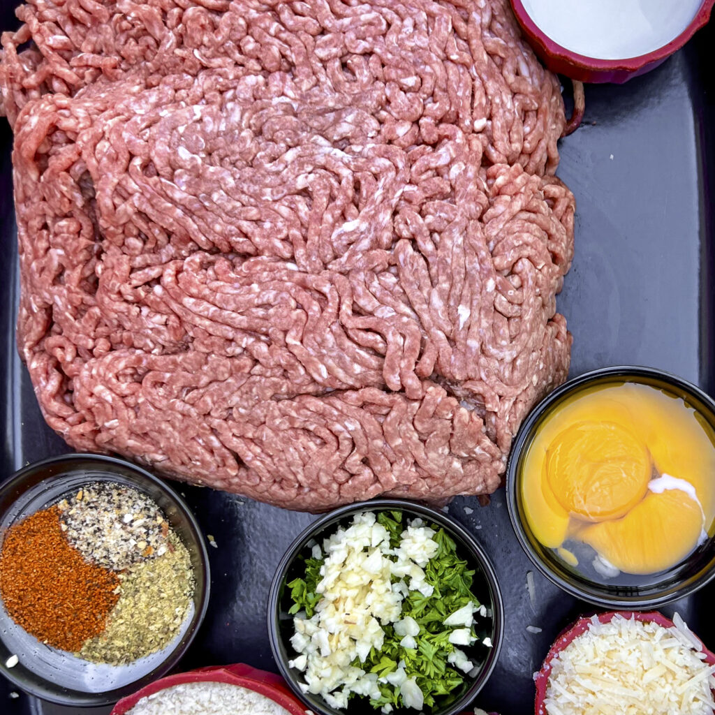Showing ground beef with the other ingredients  that go in meatballs. 