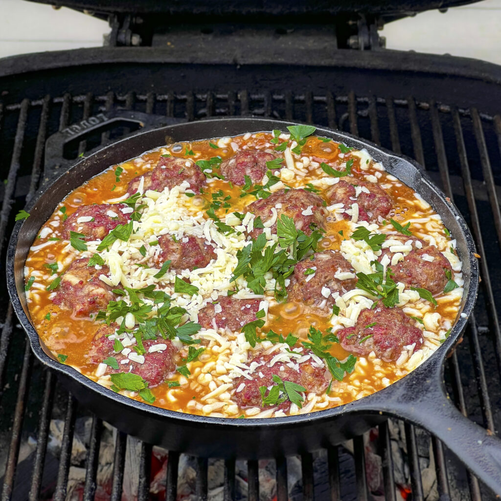 A skillet of meatballs in marinara are on the grill. 