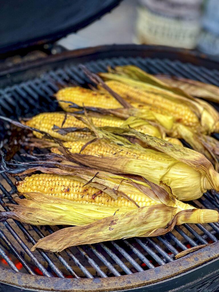 Corn in the husk is on the grill.