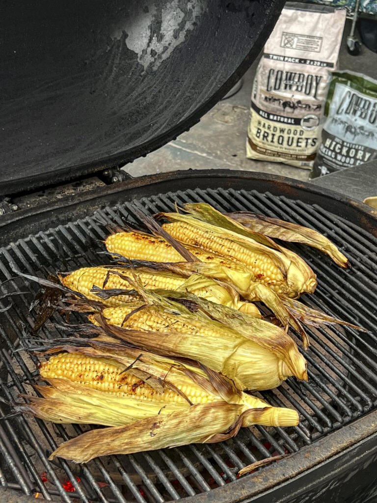 Golden Brown Grilled Corn on grill grates with Cowboy Charcoal in the back.