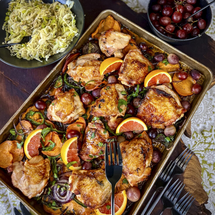A sheet pan of cooked chicken thighs with orange slices.