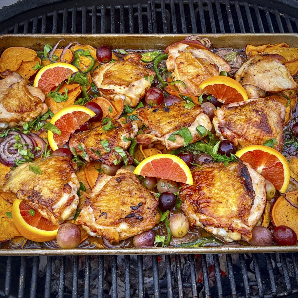 A sheet pan of chicken thighs, oranges, basil, grapes, onions, and poblano. 